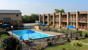 Un hotel con piscina, mobiliario de exterior y un patio cercado.