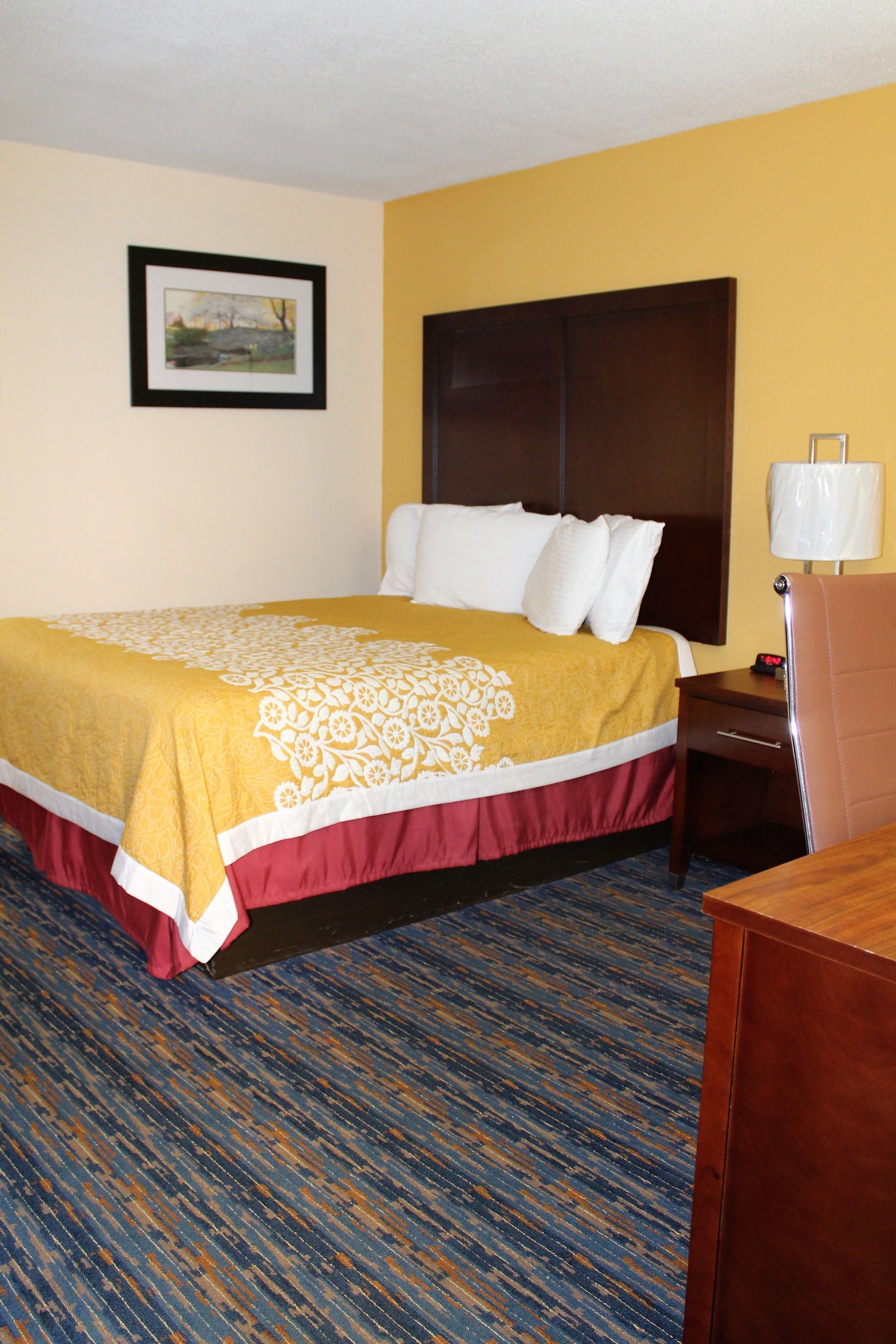 A hotel room with a bed, a nightstand, a lamp, and a framed picture on the wall.