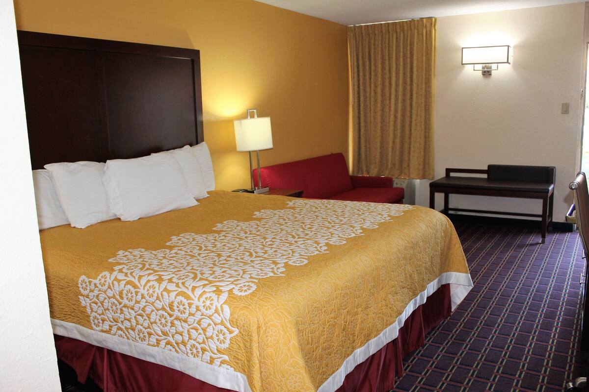 A hotel room with a large bed, a desk, a chair, a lamp, and a window with curtains.