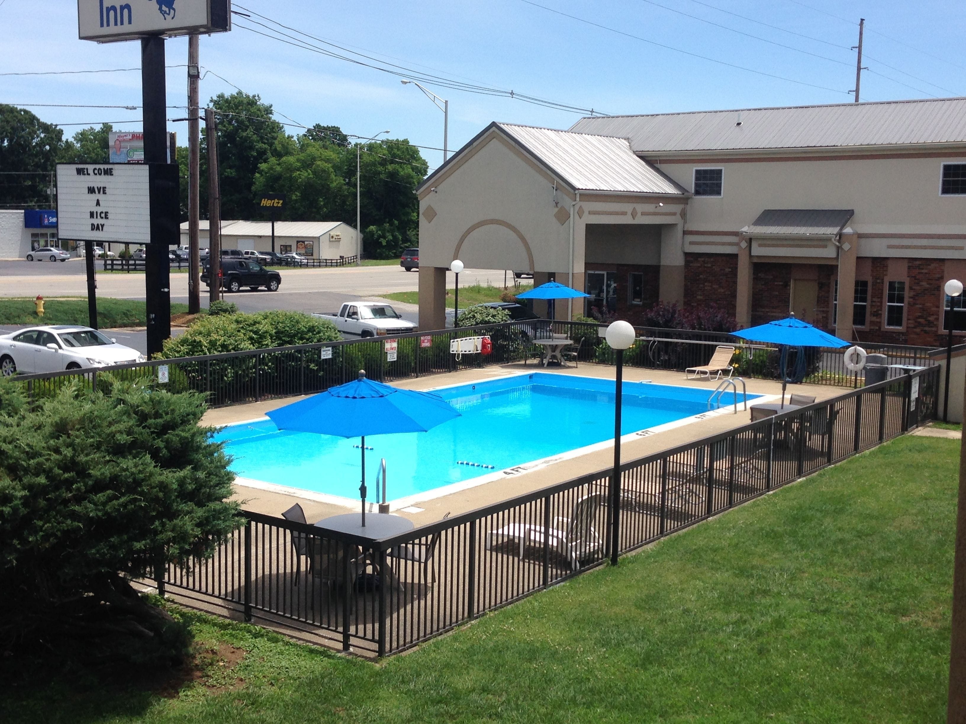 A swimming pool with a fenced deck, surrounded by a lawn and a building with a sign that reads "Inn".