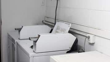 Une buanderie équipée de deux machines à laver, d’un étendoir et d’un panneau indiquant que du détergent est disponible au bureau.