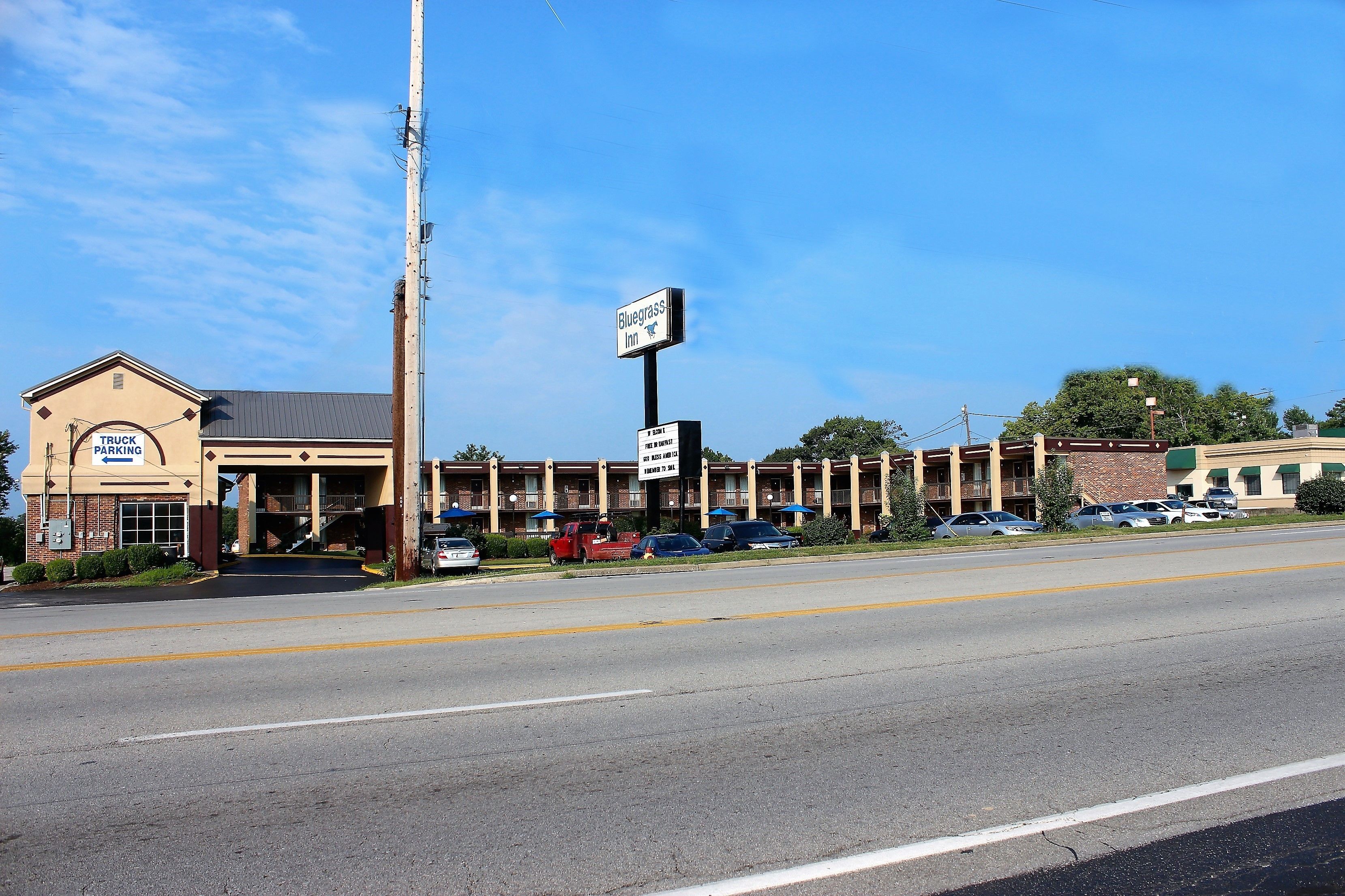 Un motel avec un panneau indicateur, un parking et une route devant.