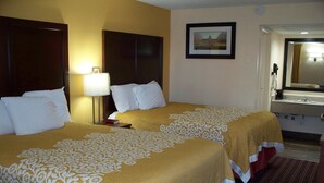 A hotel room with two beds, a nightstand, a lamp, a framed picture on the wall, and a bathroom visible through an open door.