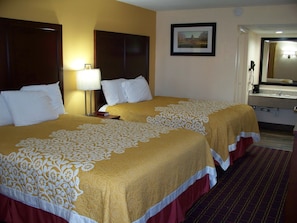 A hotel room with two beds, a nightstand, a lamp, a framed picture on the wall, and a bathroom visible through an open door.