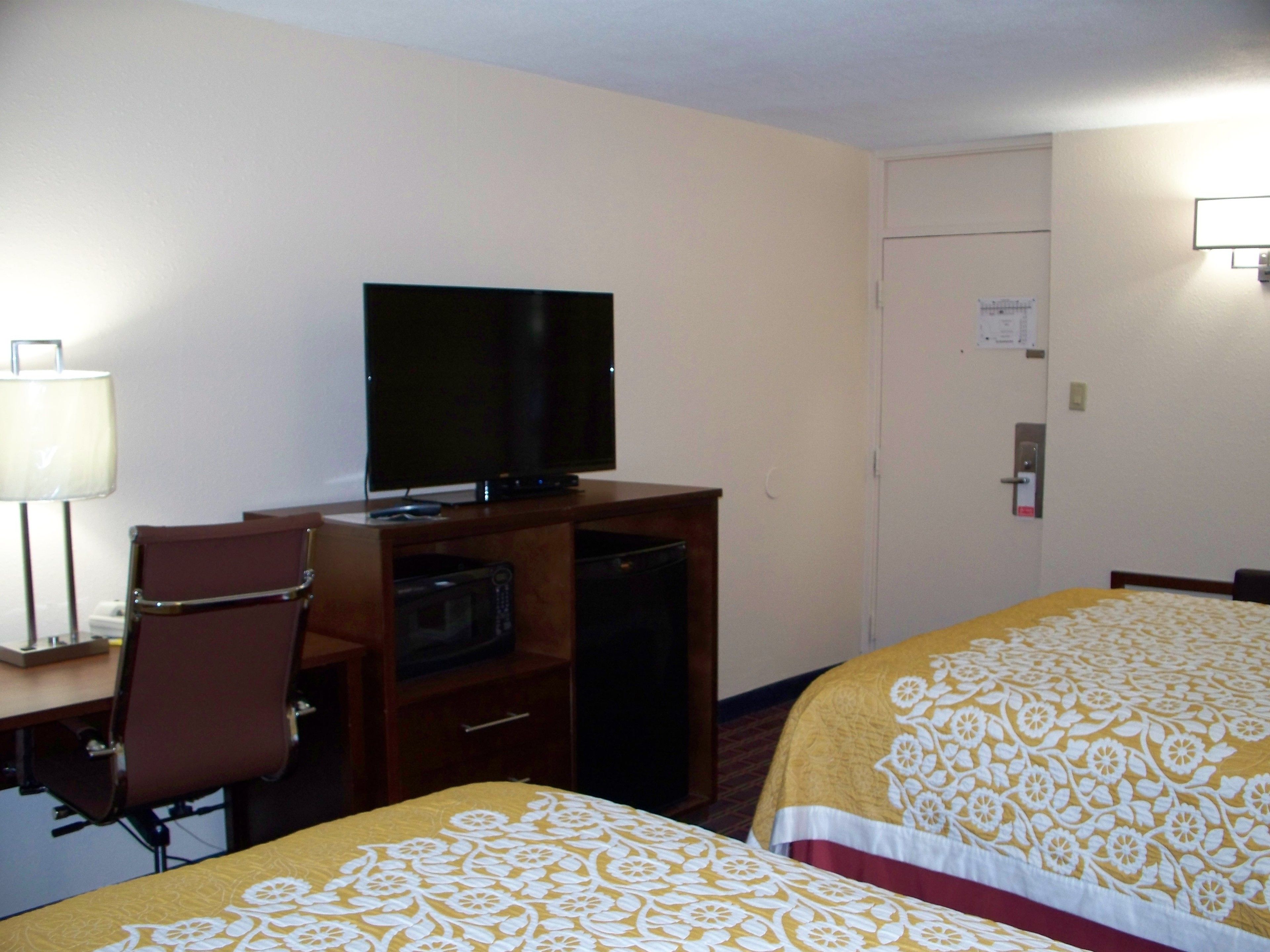 A hotel room with a bed, a desk with a television, a microwave, and a chair.