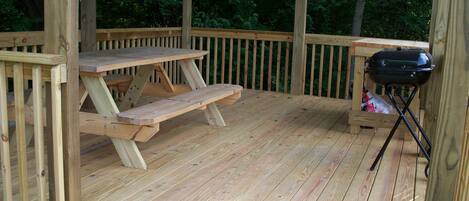Una terraza de madera con una mesa de picnic y una parrilla portátil.