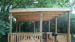 Una terraza de madera con techo de pérgola, una parrilla y un banco.