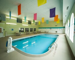 Una piscina interior con agua azul cristalina, rodeada de sillones de descanso y mesas, con banderas de colores colgando del techo.