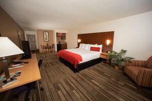 Habitación de hotel con una cama grande, un escritorio con computadora, una silla, una pequeña kitchenette y un sofá.