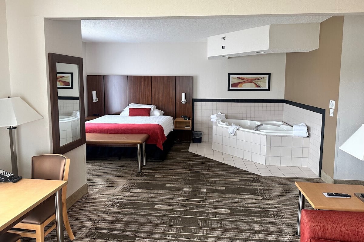 A hotel room with a bed, a desk, a chair, a bathroom with a bathtub, and a mirror.