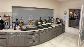 A kitchen area with a coffee machine, fruit bowl, and various food containers.