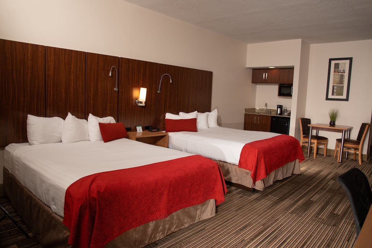A hotel room with two beds, a kitchenette, a dining area, and a bathroom.