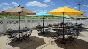 Outdoor patio seating with tables and chairs, surrounded by a white fence, under umbrellas. - Northfield Inn, Suites & Conference Center (Springfield)