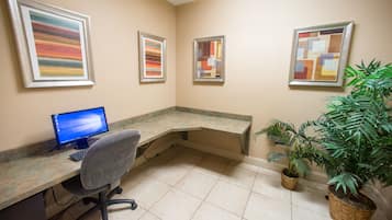 A room with a desk, computer, chair, and three framed artworks on the wall.