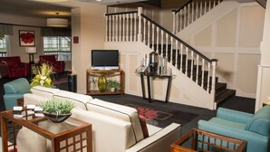 A spacious living room with a sofa set, a coffee table, and a television. A staircase with a railing is visible in the background. - Northfield Inn, Suites & Conference Center (Springfield)