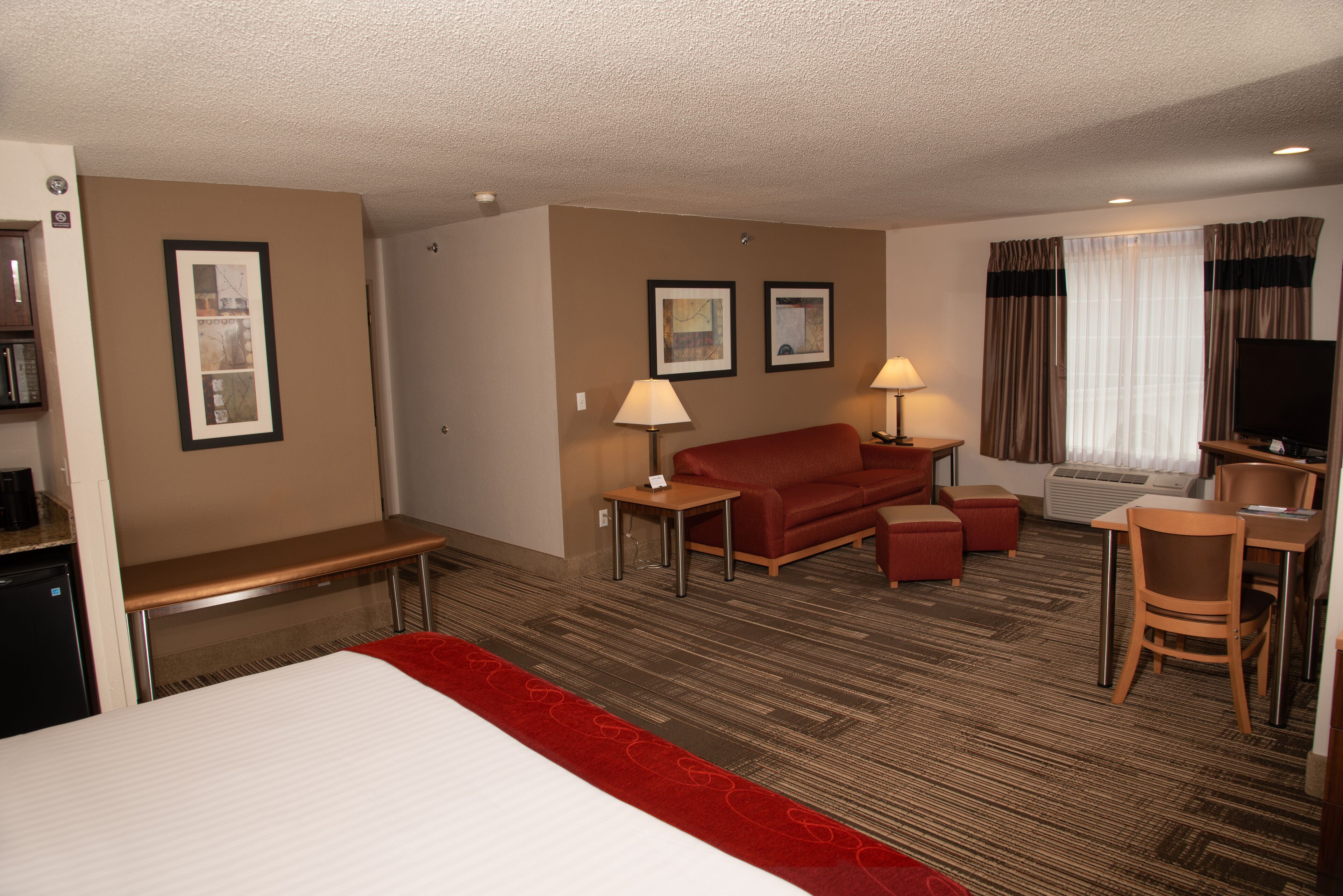 A hotel room with a bed, a red sofa, a small table, a chair, and a desk.