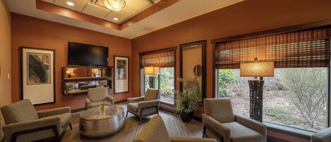 Un salón amplio con televisión de pantalla plana, asientos cómodos, una mesa de centro y ventanas grandes con persianas.