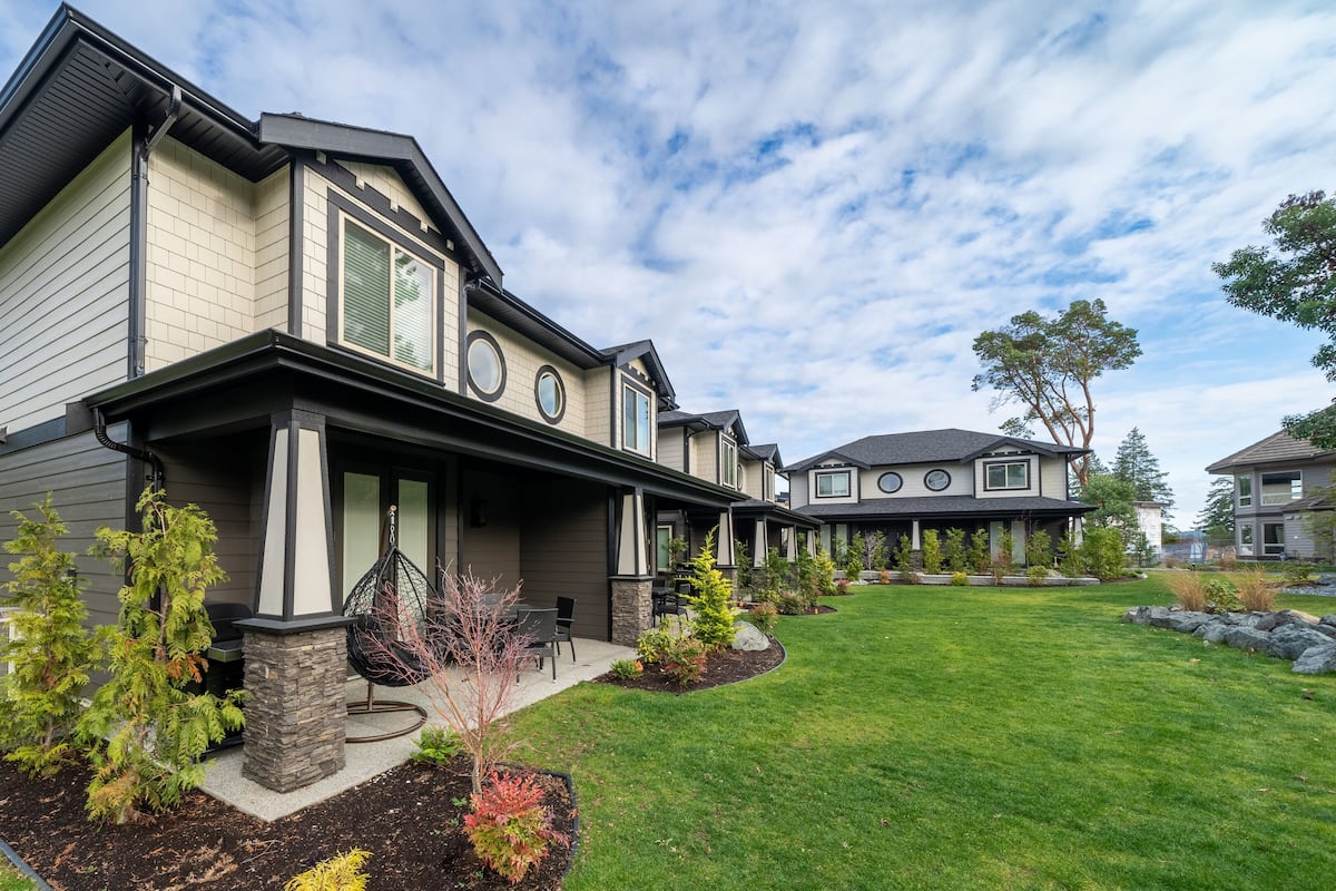 A modern two-story house with a covered porch, stone pillars, and a well-maintained lawn.