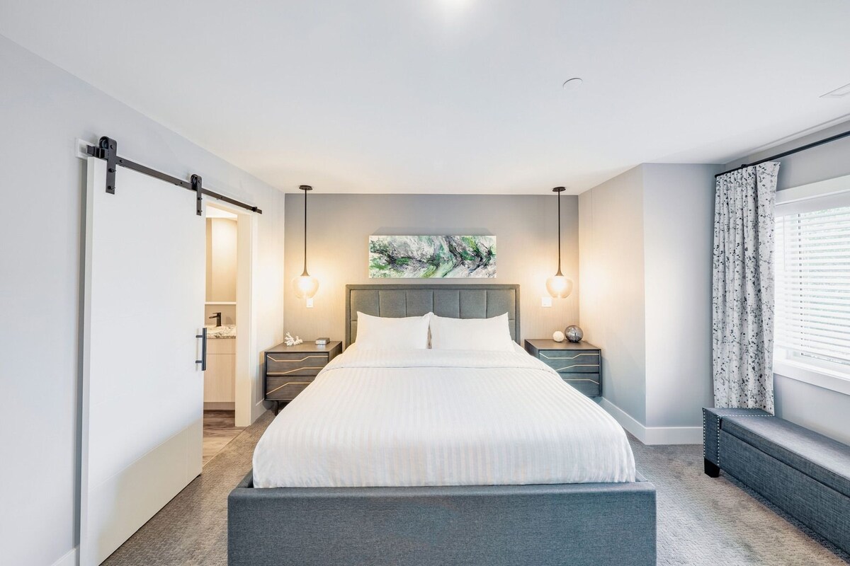 A modern bedroom with a large bed, bedside tables, a bench, and a painting on the wall.