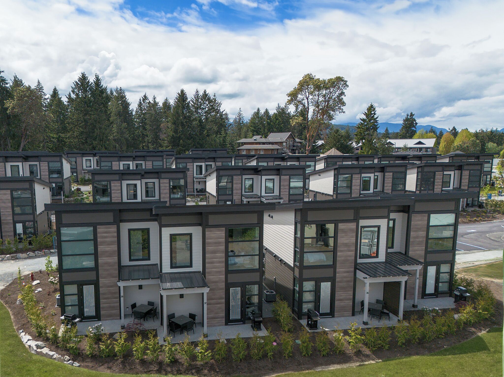 A modern residential complex with multiple two-story houses featuring large windows, outdoor patios, and a landscaped garden area.