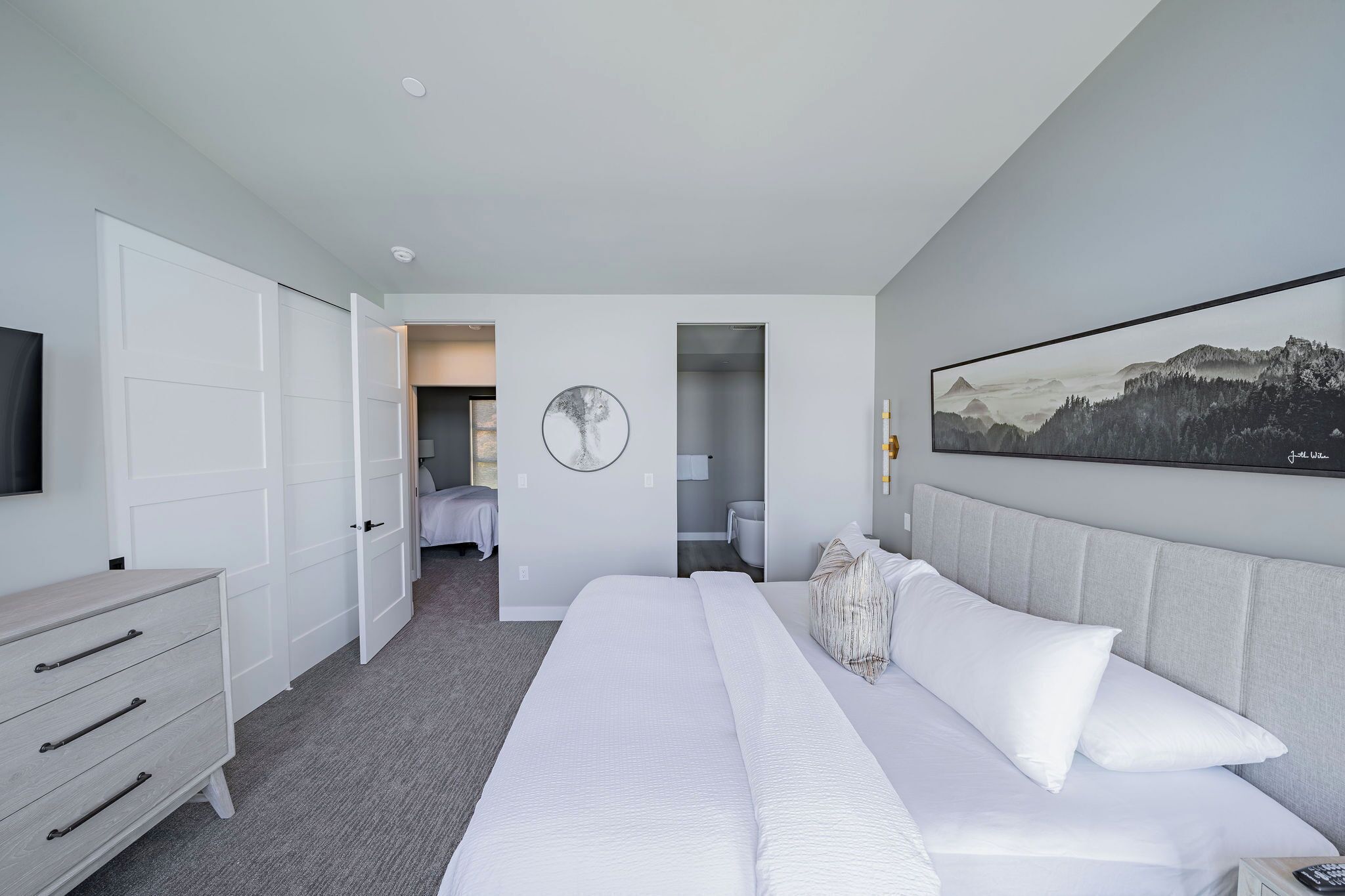 Una habitación de hotel moderna con una cama grande, un aparador, un televisor y un cuadro en la pared.