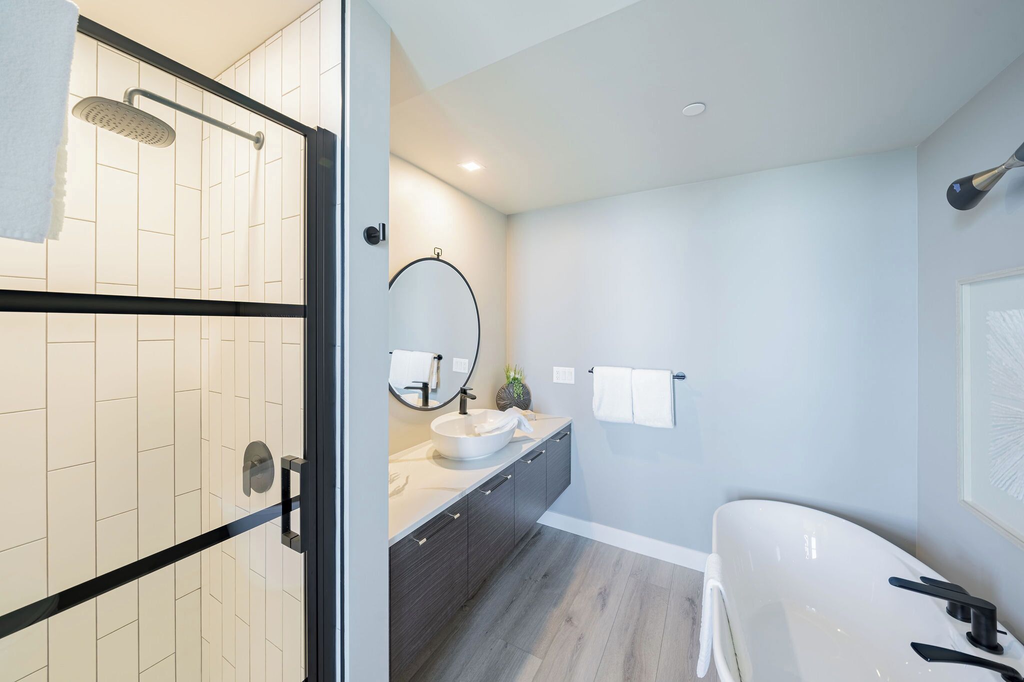 A modern bathroom with a glass shower enclosure, a white sink, dark cabinetry, and a large mirror.