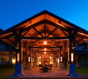 A covered outdoor area with a wooden roof, a central seating area, and a stone wall.