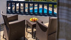 Un balcon agrémenté de meubles en osier, une piscine et une vue sur une plage et des montagnes.