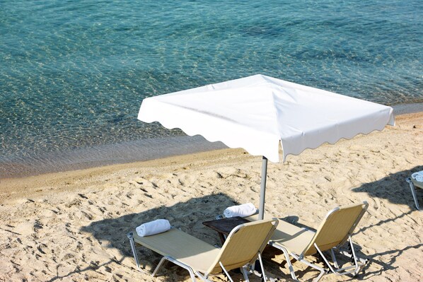 A beach with clear water, two sun loungers, and a white umbrella.