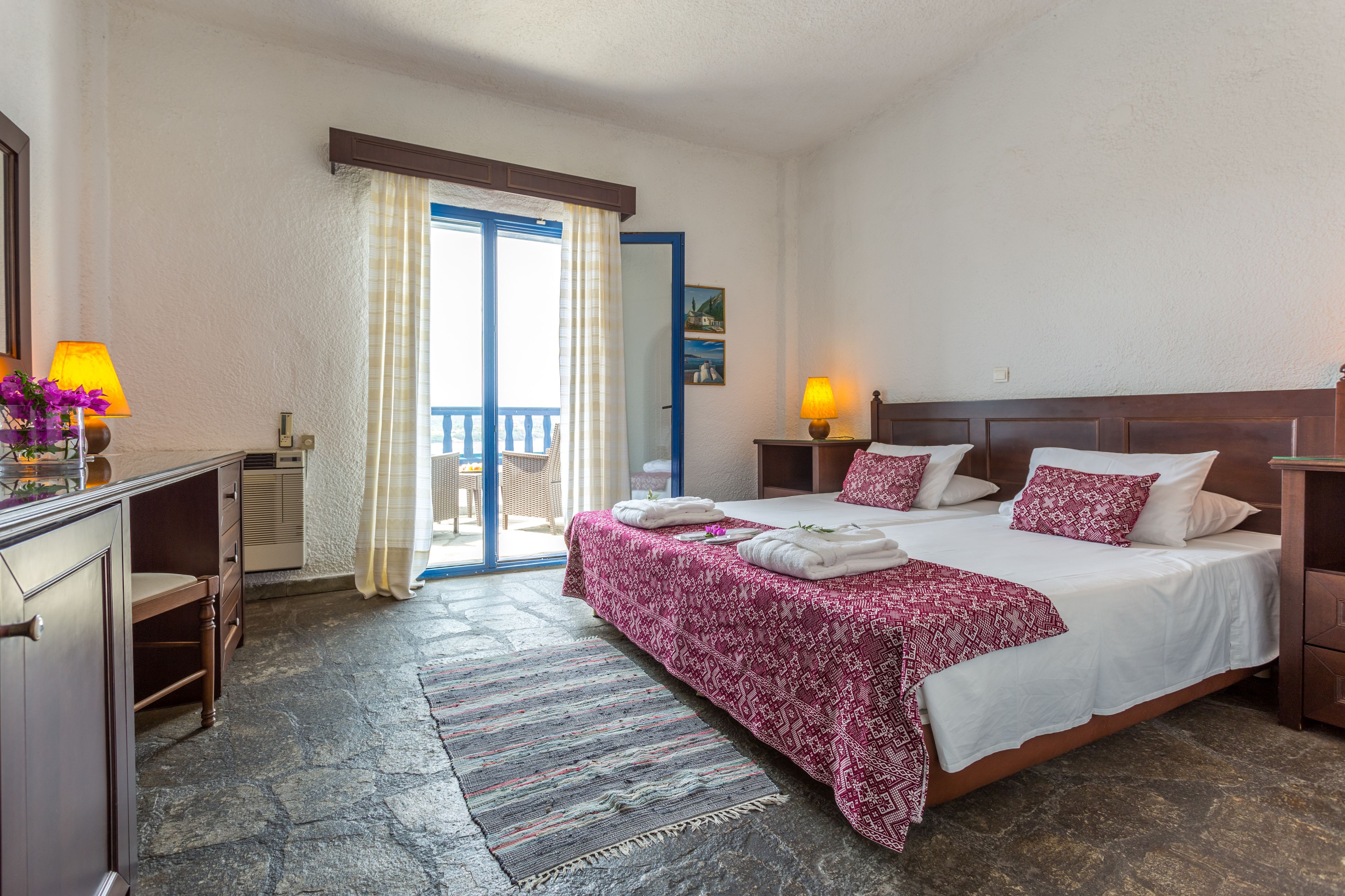 Una camera d'albergo con un letto grande, due comodini con lampade, una scrivania con una sedia, un armadio, un bagno con doccia e un balcone con vista.