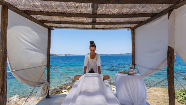 Une séance de massage en plein air, sur une plage, sous une pergola en bois, avec vue sur la mer.