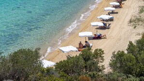 Une plage aux eaux turquoise et limpides, parsemée de parasols blancs, où quelques personnes se détendent.