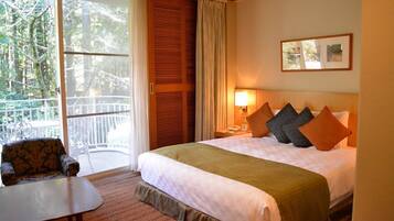 Hotelkamer met een groot bed, een bureau, een stoel, een balkon met uitzicht op bomen en een ingelijst schilderij aan de muur.
