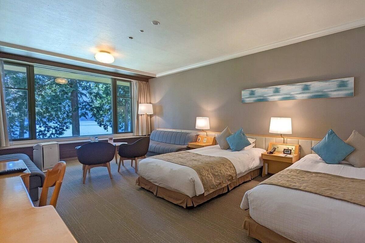 Habitación de hotel con dos camas, un escritorio y una silla. Hay lámparas en cada mesita de noche y un cuadro en la pared.