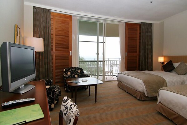 A hotel room with a TV, a sofa, a table, a bed, and a balcony with a view.
