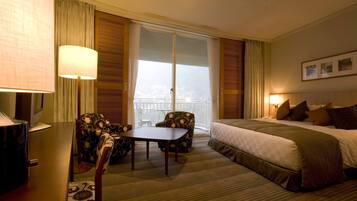Hotelkamer met een bed, een bureau, twee stoelen, een tafel en een groot raam met gordijnen.