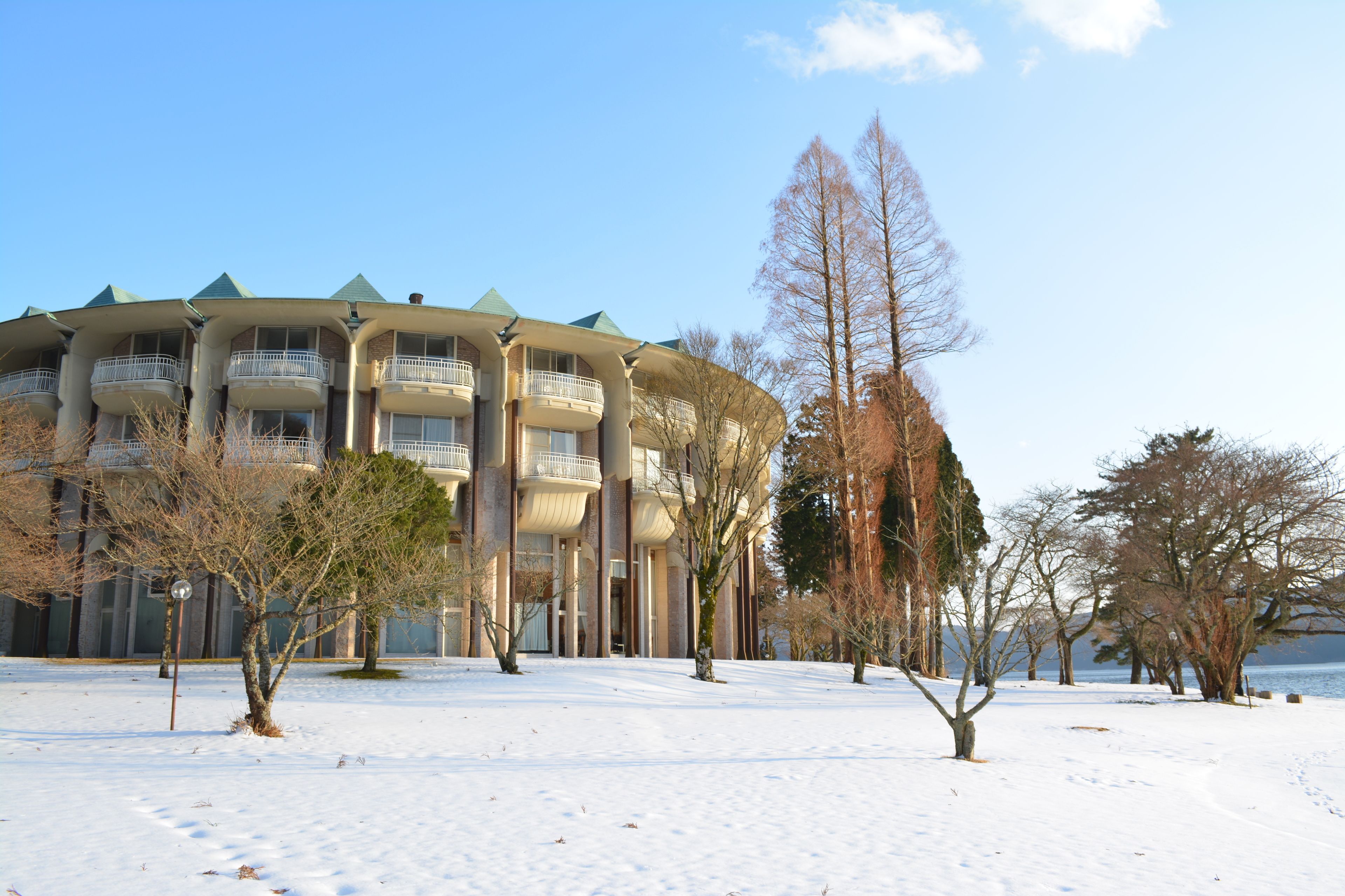 Un immeuble à plusieurs étages doté de balcons, entouré d’un paysage enneigé et d’arbres sans feuilles.
