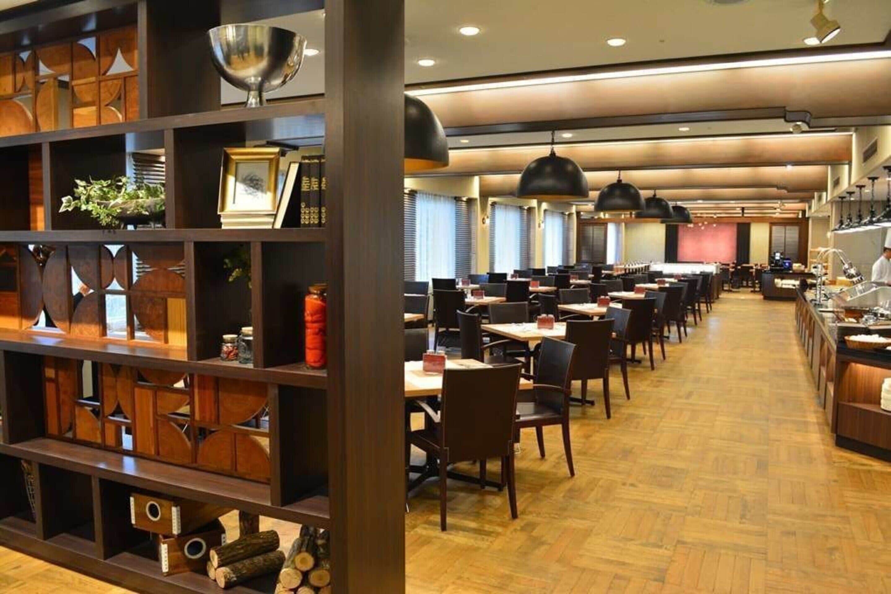 Un restaurante espacioso con varias mesas y sillas, suelo de madera e iluminación colgante.