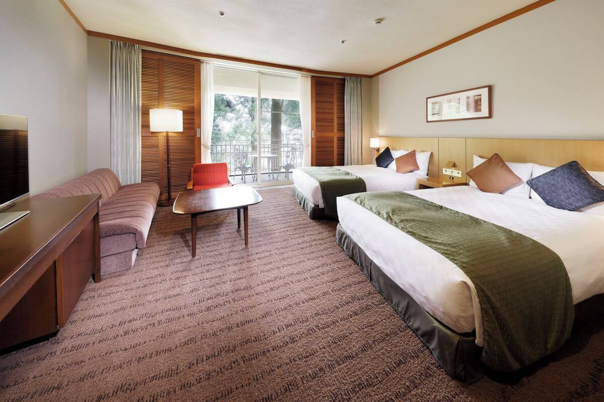 Habitación de hotel con dos camas, un sofá, una mesita y un televisor.