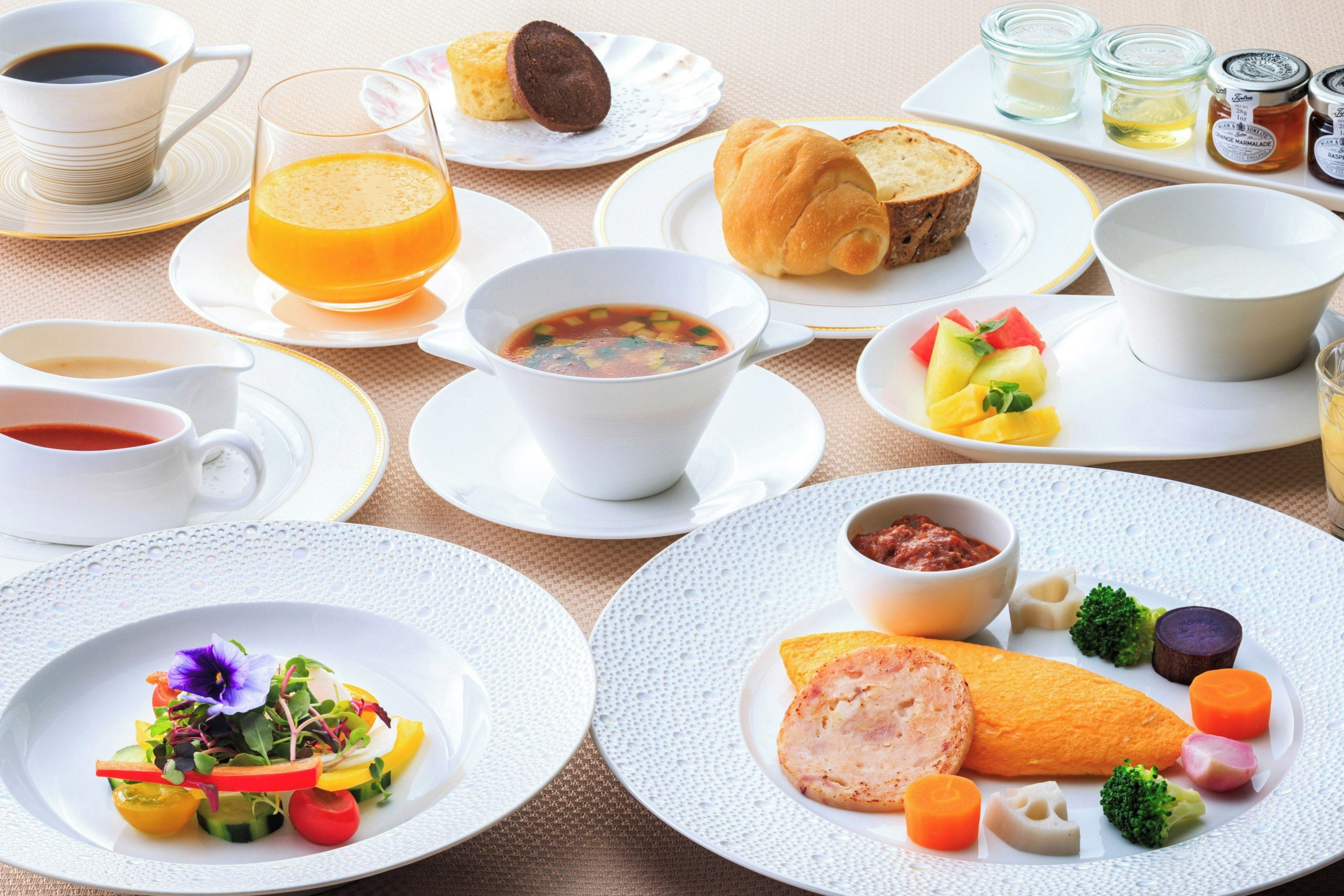 A table set with various breakfast items including soup, bread, fruit, and a salad.