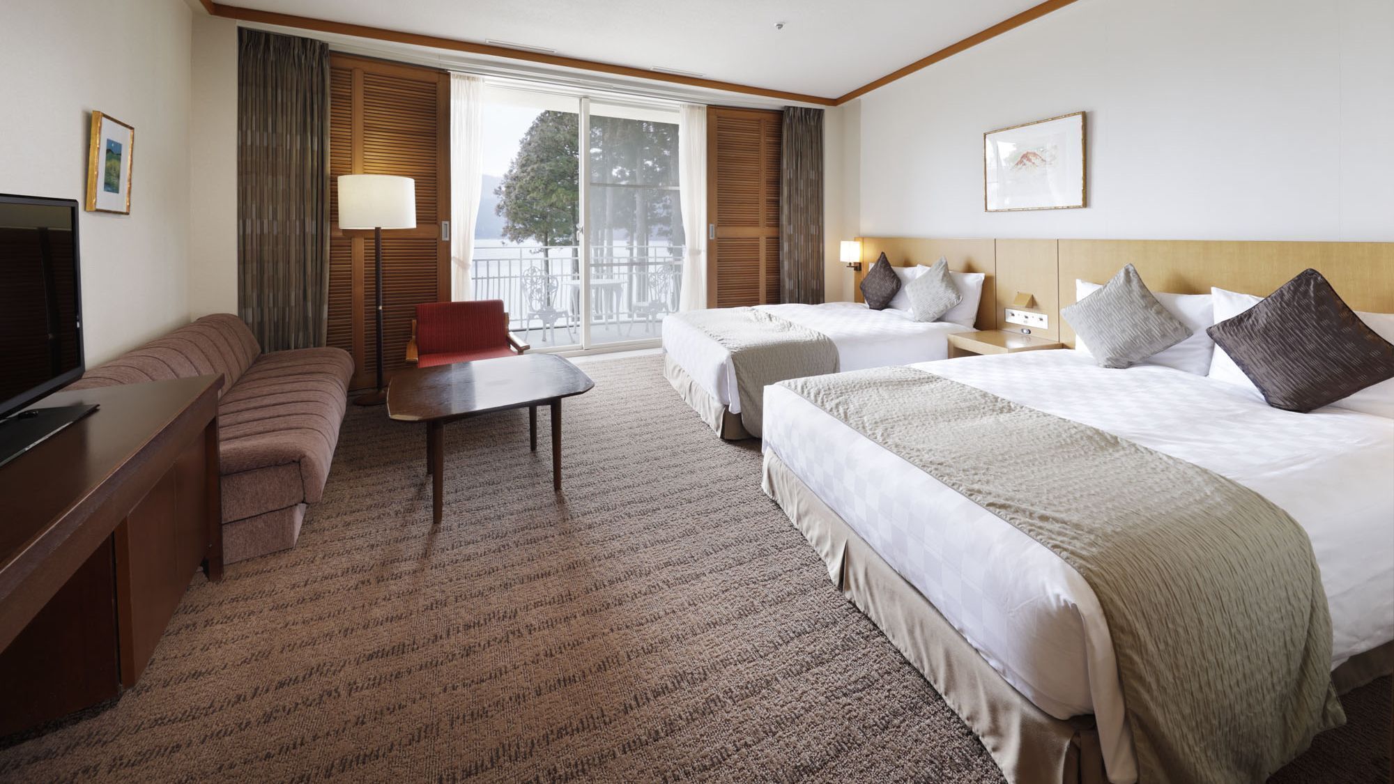 Ein Hotelzimmer mit einer Couch, einem kleinen Tisch, zwei Betten, einem Fernseher und einem Fenster mit Blick.