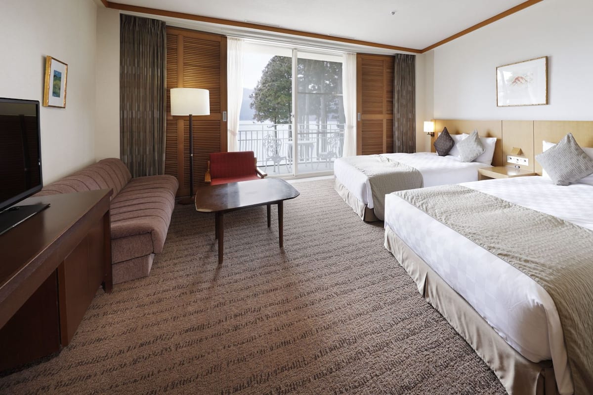 Habitación de hotel con sofá, una mesita, dos camas, televisión y ventana con vistas.