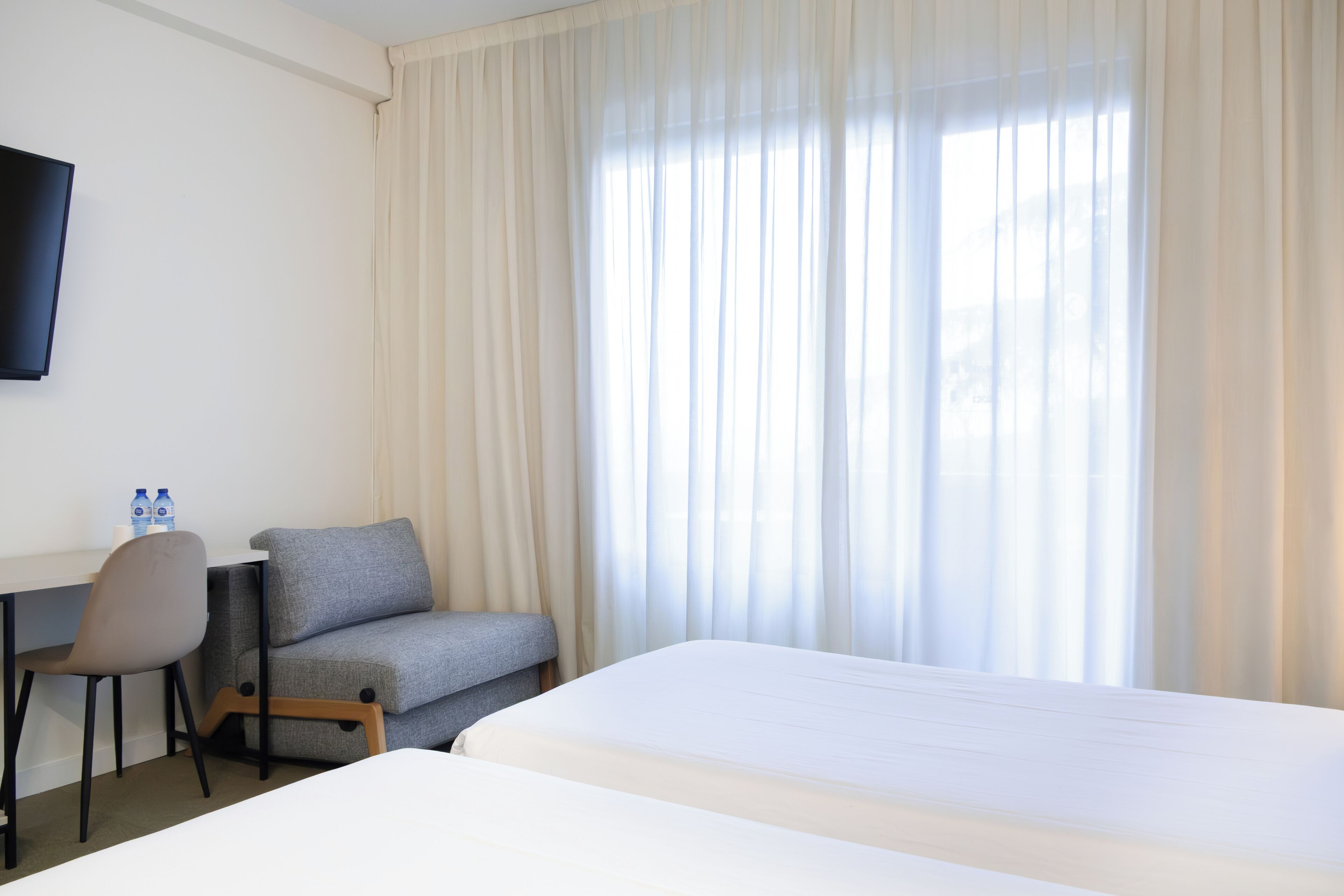 A hotel room with a bed, a desk, a chair, and a TV.