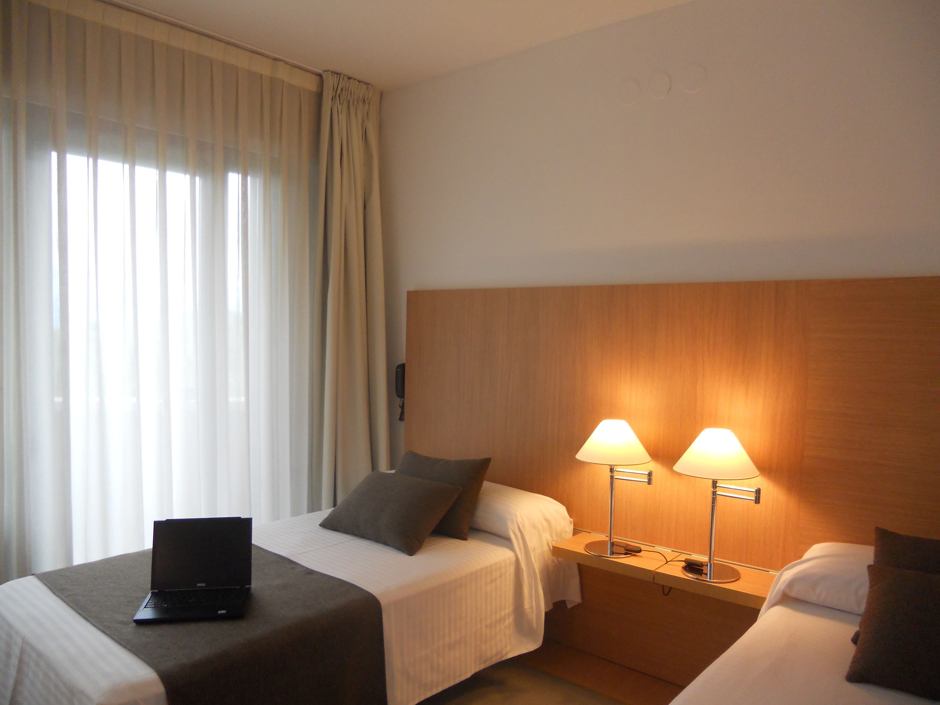 Une chambre d’hôtel avec deux lits, un bureau, un ordinateur portable et deux lampes de chevet.