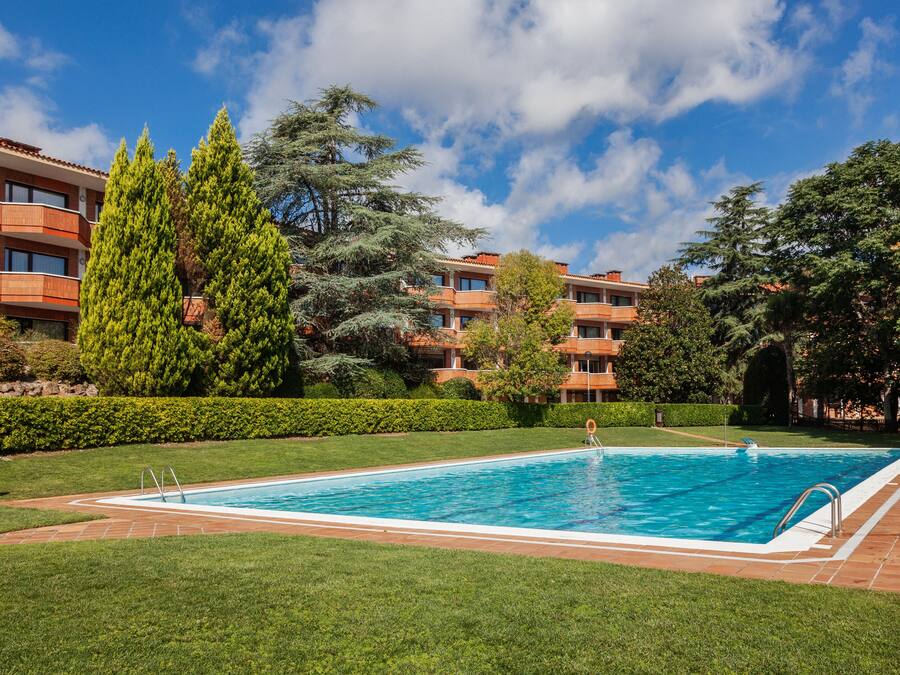 A rectangular swimming pool with a tiled deck, surrounded by well-maintained grass and trees.