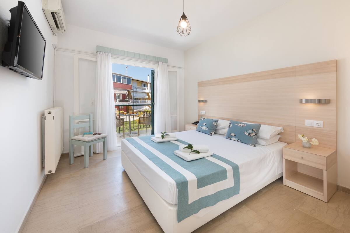A bedroom with a bed, bedside table, chair, and a TV mounted on the wall.