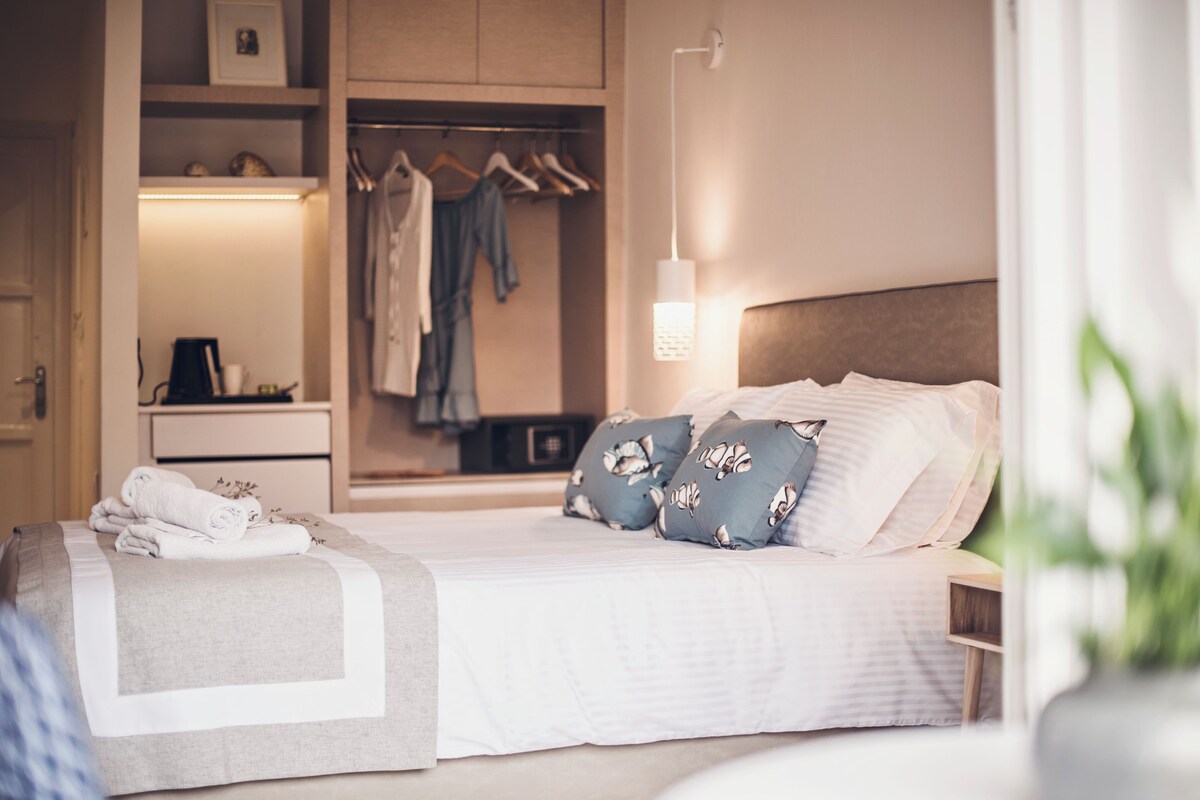 Una cama bien hecha con almohadas, una mesita de noche, un armario y un closet con ropa.