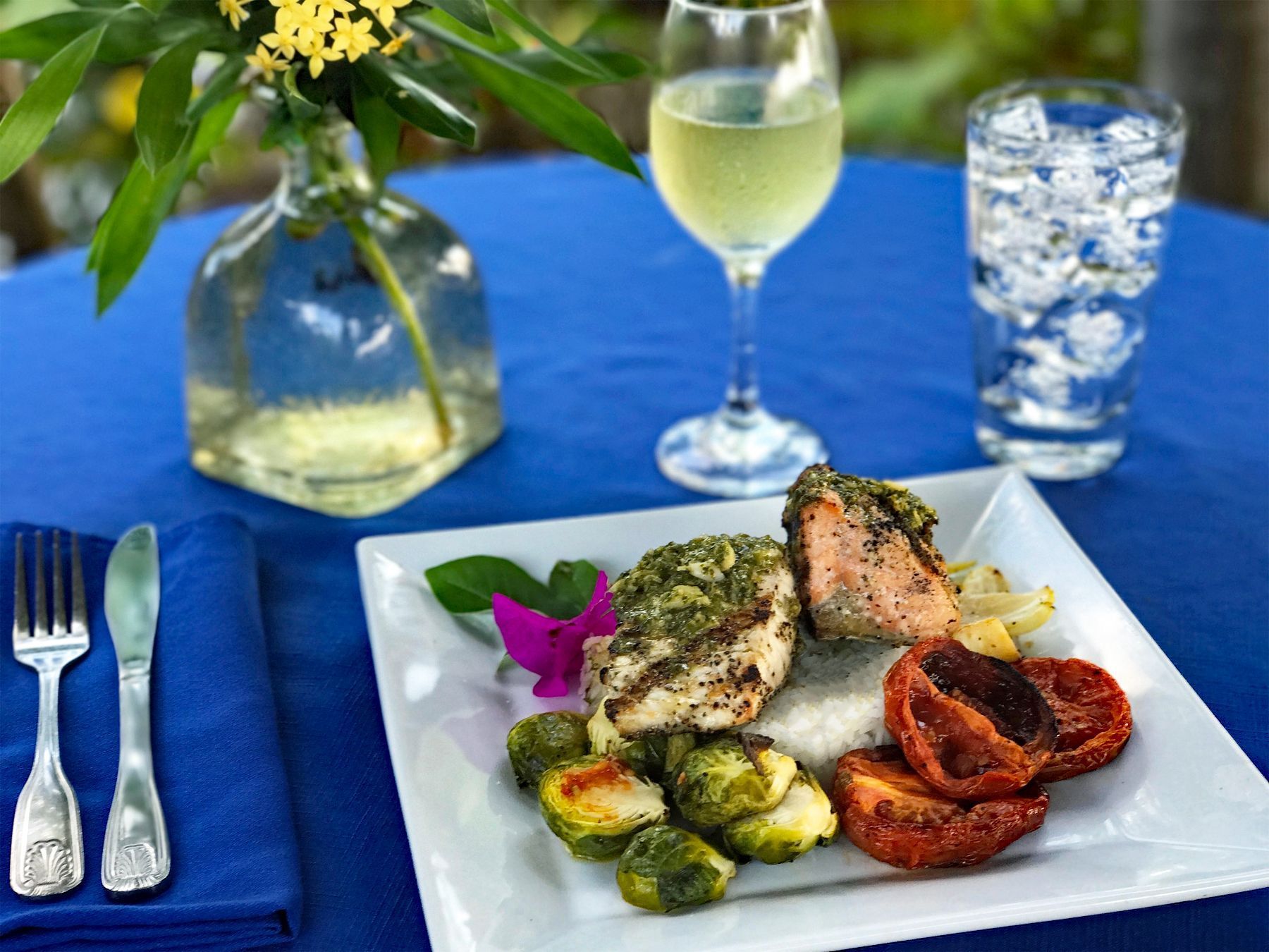 A plate of food with a glass of white wine and a glass of water on a blue tablecloth.