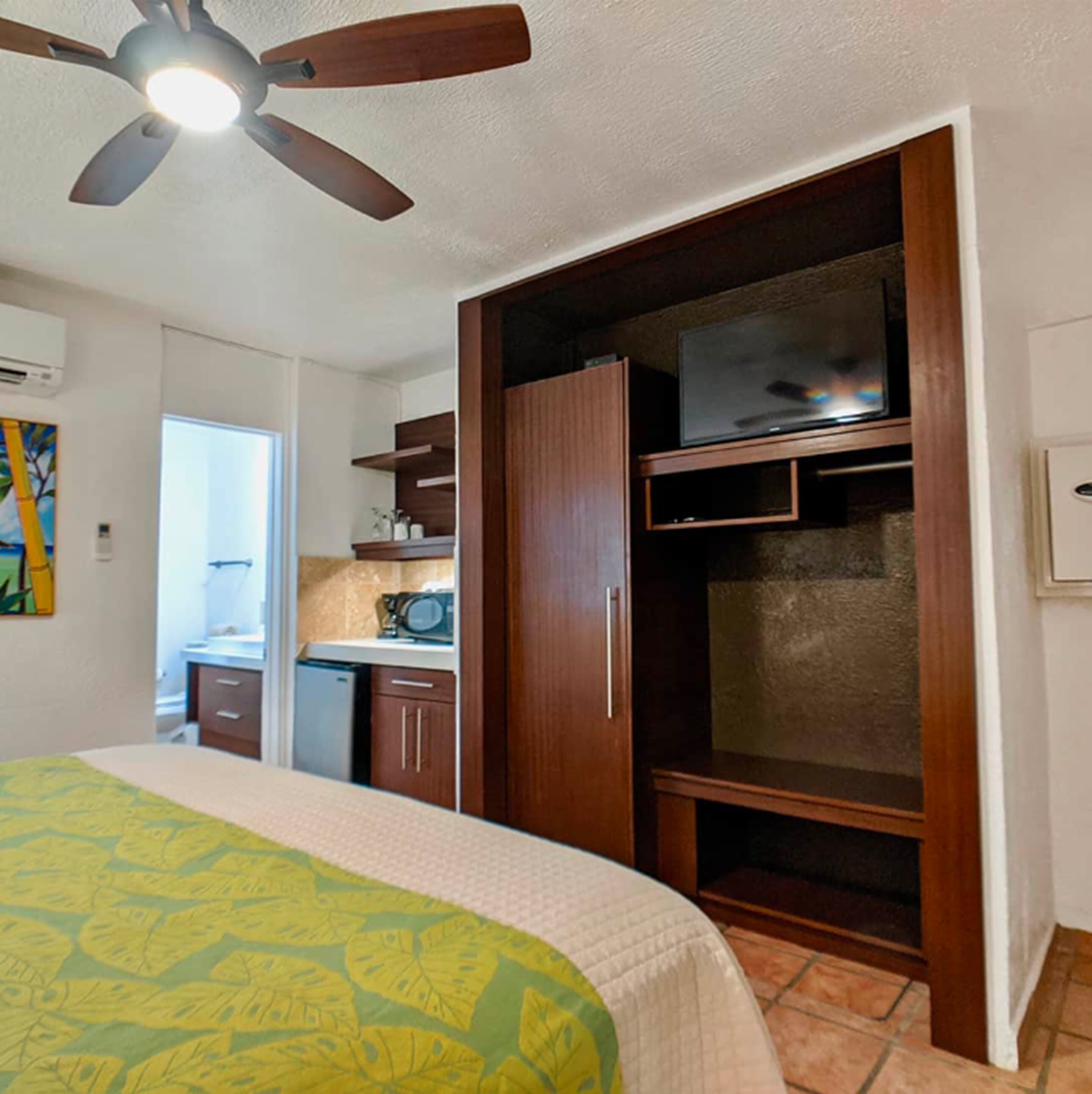 Une chambre avec un lit, un ventilateur de plafond, un coin cuisine et un téléviseur.