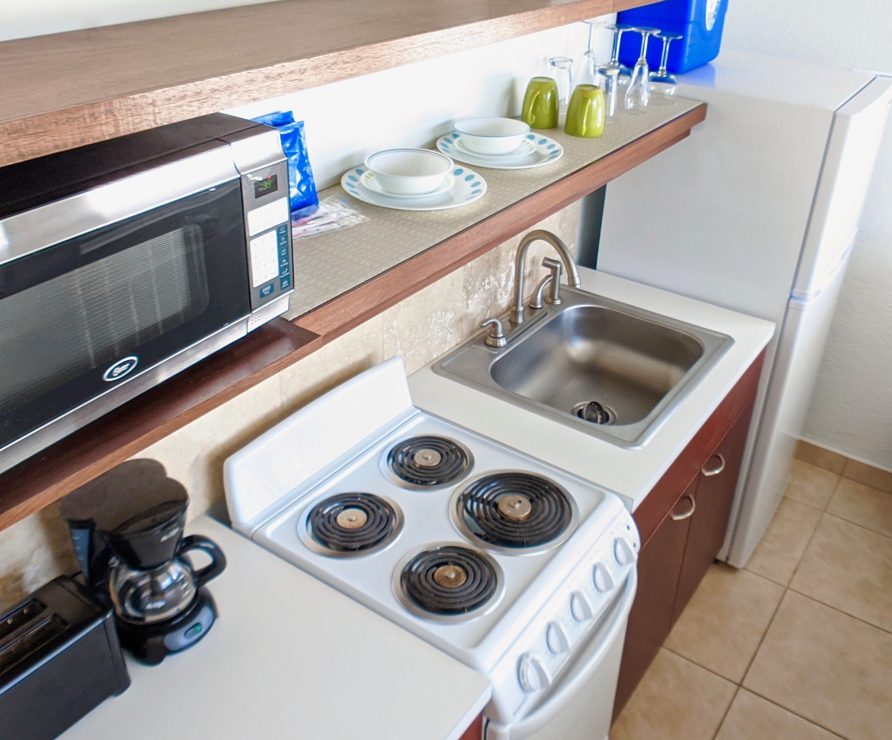 A compact kitchen with a microwave, stove, sink, and coffee maker.